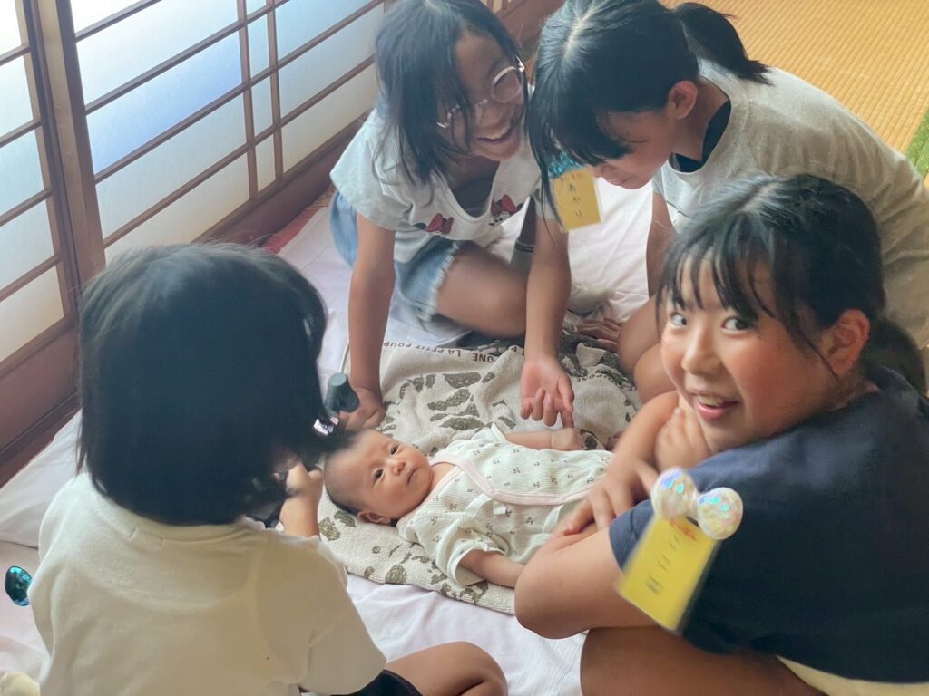 こどもおぢばがえり詰所で、子供達が囲むのは2ヶ月経たないめぐみちゃんです。